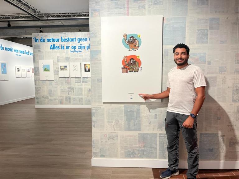 Sameh Samir standing beside his cartoon artwork at the annual Golden Hat cartoon exhibition in Knokke, Belgium.