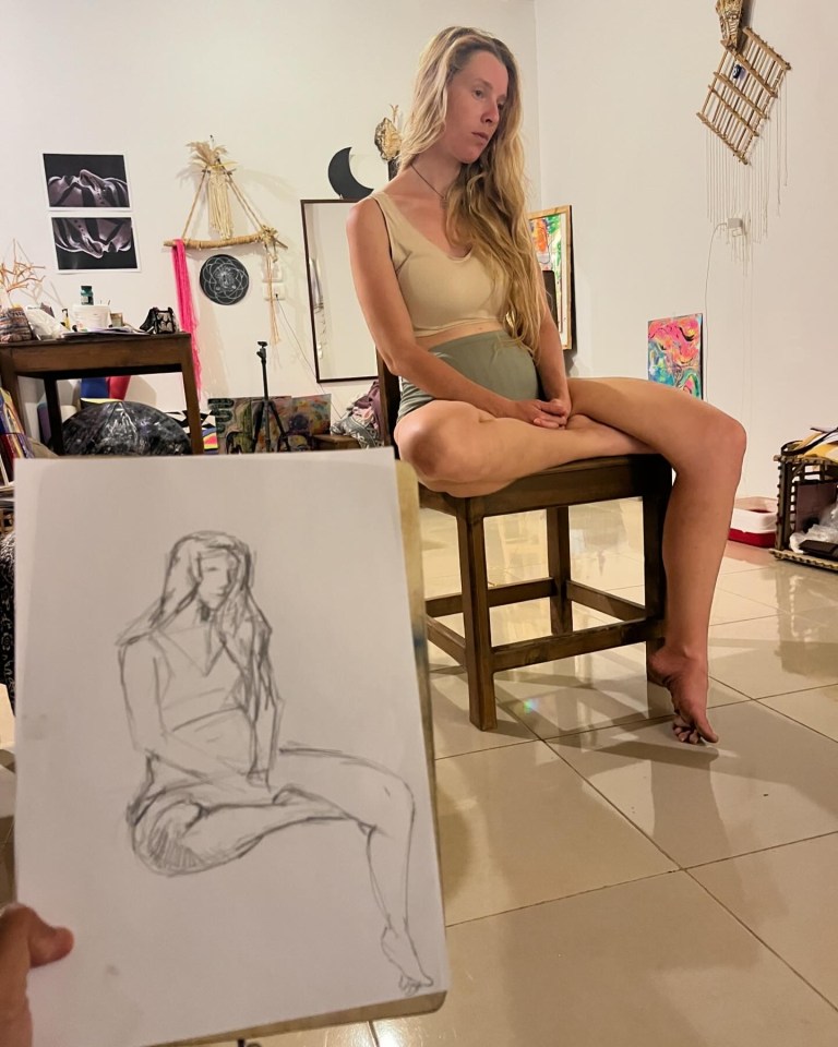 A person sketching a model sitting on a stool in an art studio.