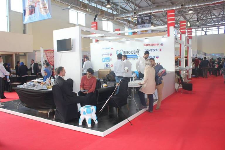 Exhibition booth with people interacting and Sameh Samir branding displayed.