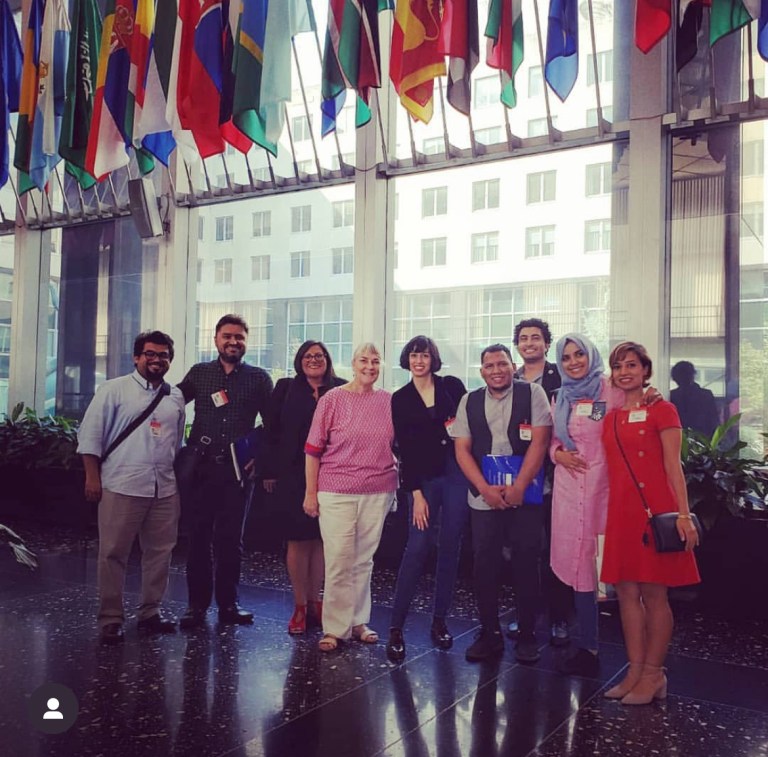 Cartoonists and colleagues at the US State Department with international flags in the background.