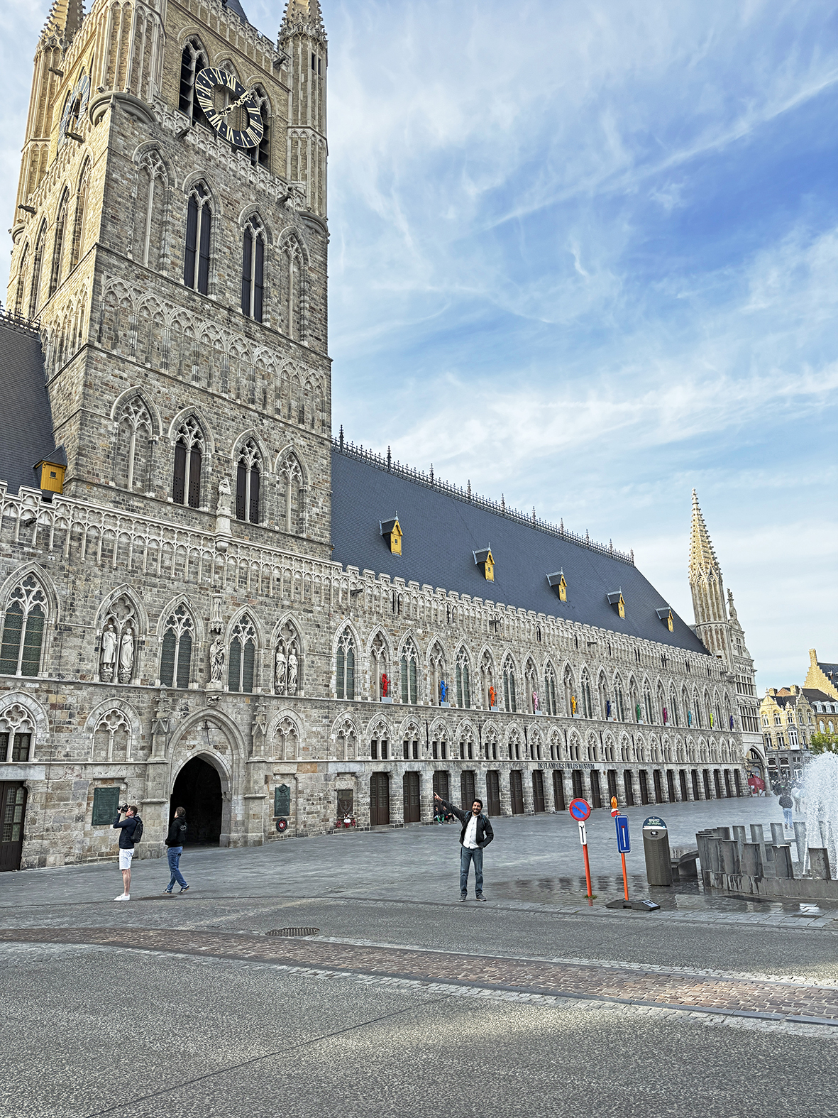 Historic clock tower in Ieper, Belgium with people walking in front.