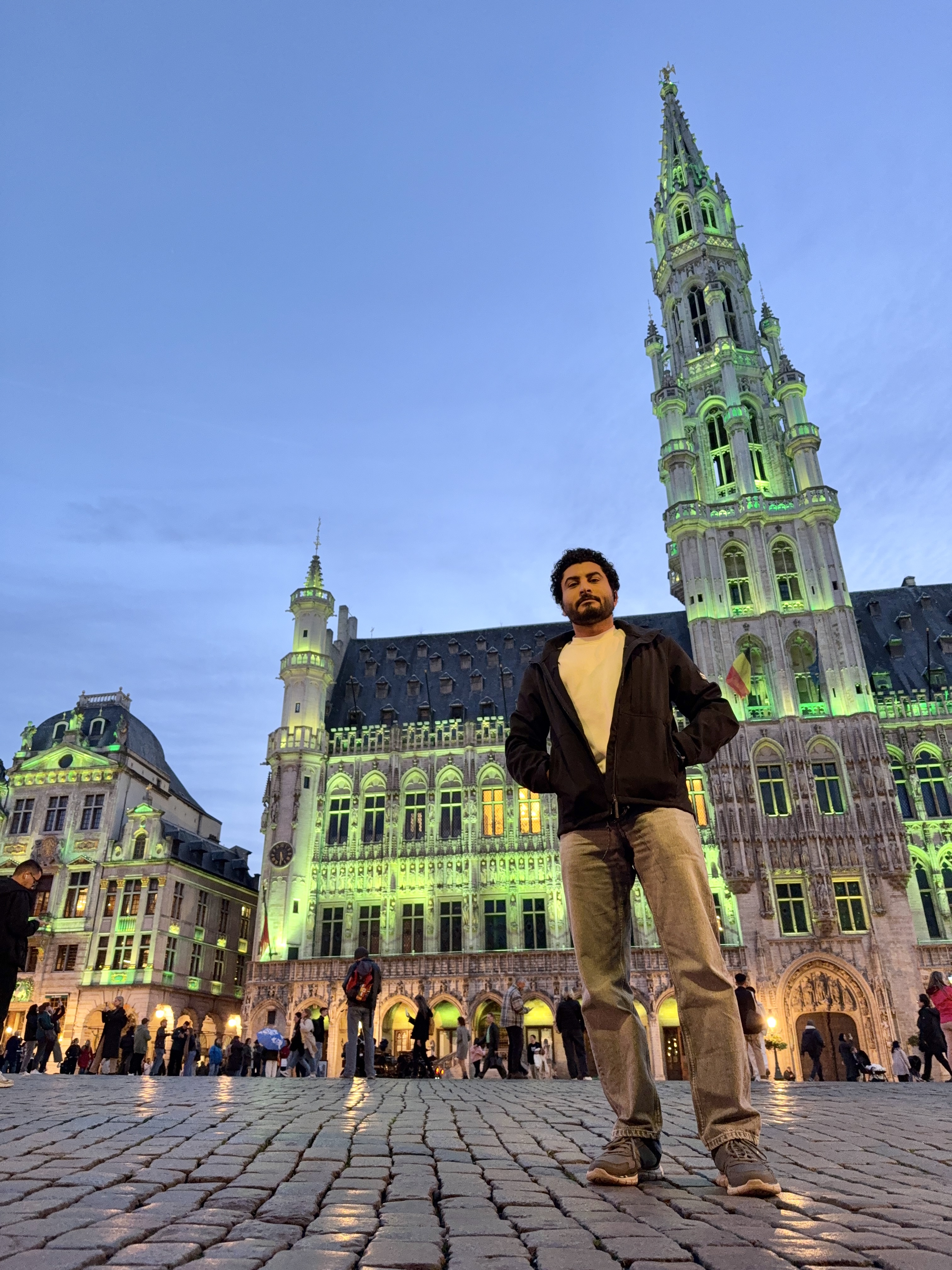 Sameh Samir standing in Brussels market square in front of a historic building illuminated with green lighting at night