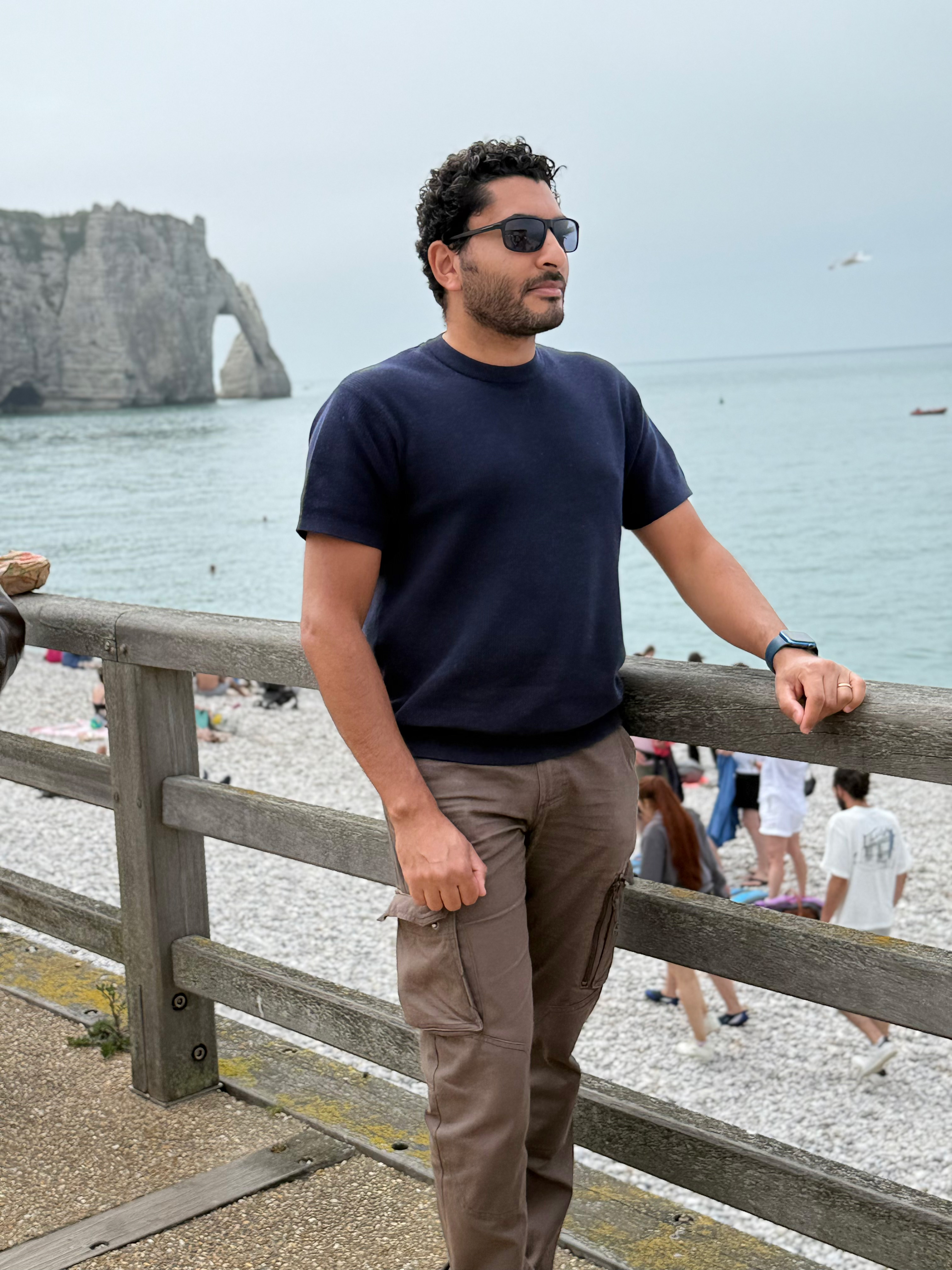 Sameh Samir standing by a seaside railing with Normandy cliffs in the background
