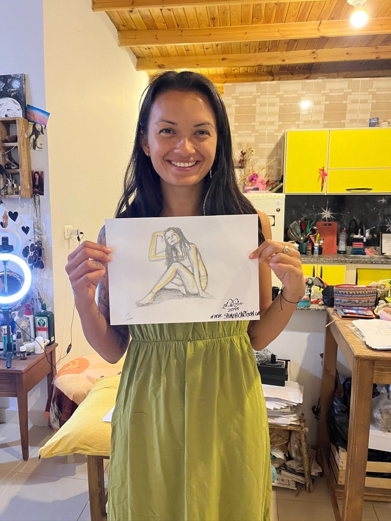 Woman holding a drawing of herself in a cozy room, smiling gently.