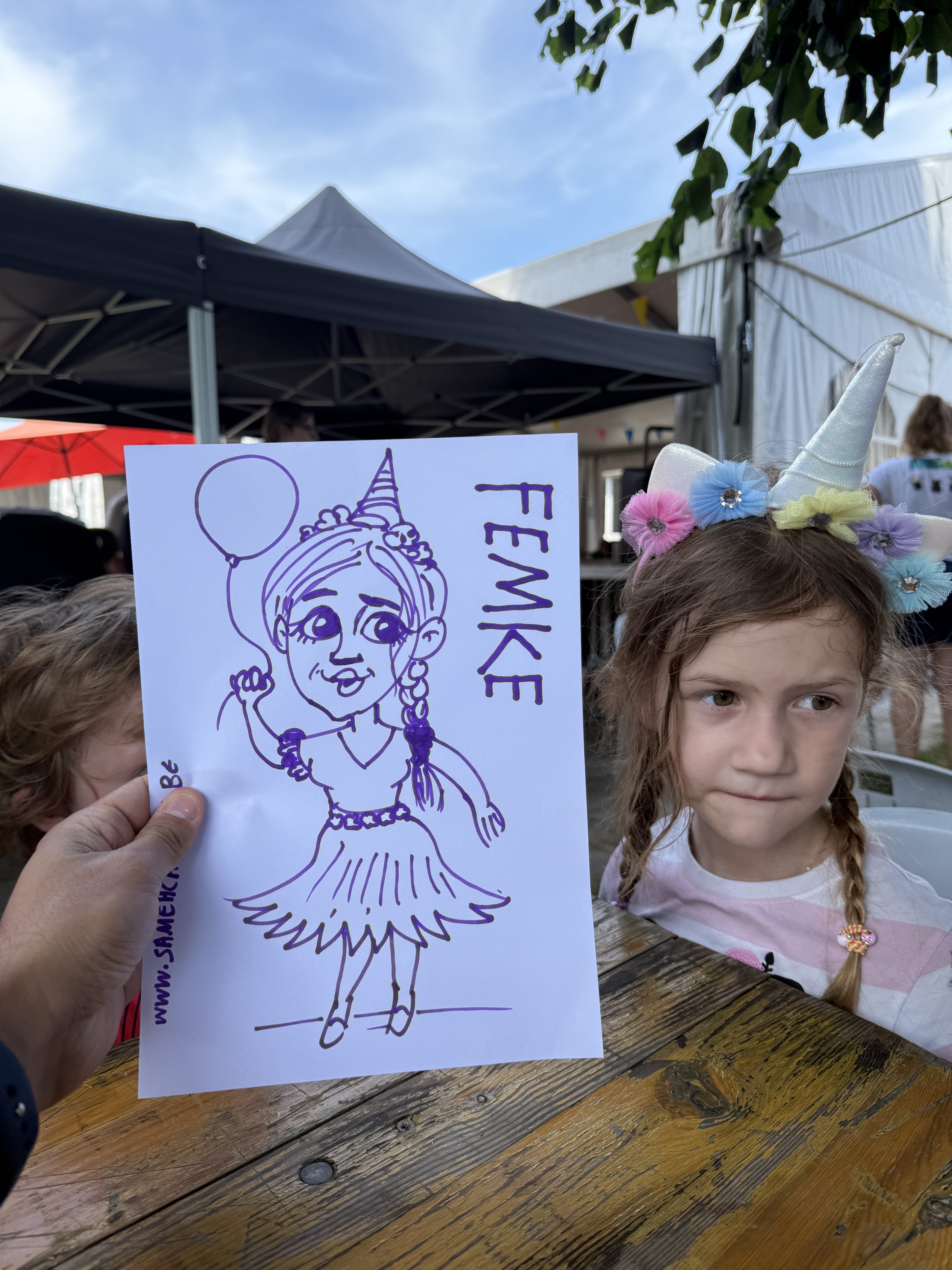 Child with her unicorn-themed live caricature at an outdoor event in Belgium