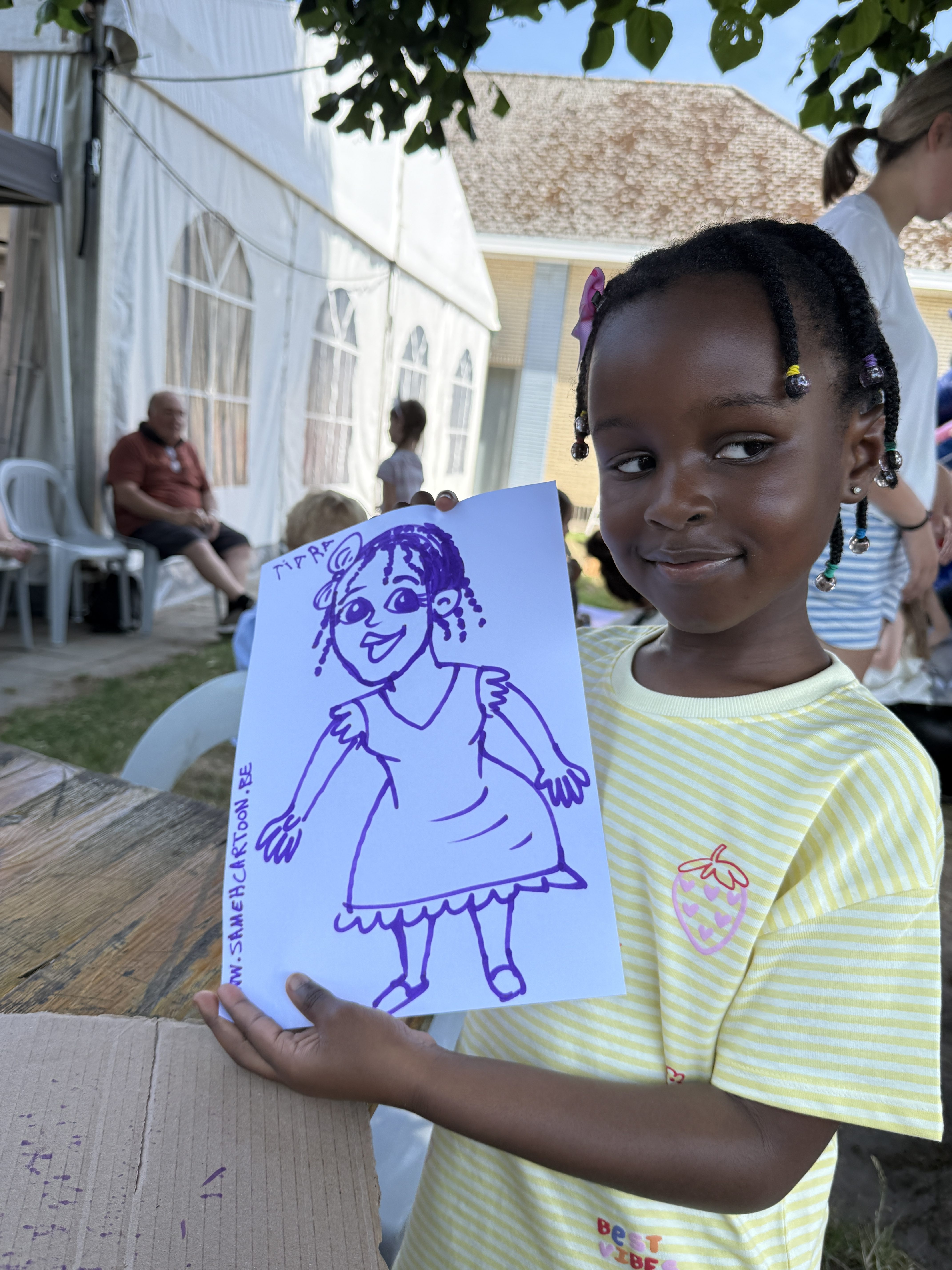 Child displaying her finished live caricature at an outdoor school celebration in Belgium