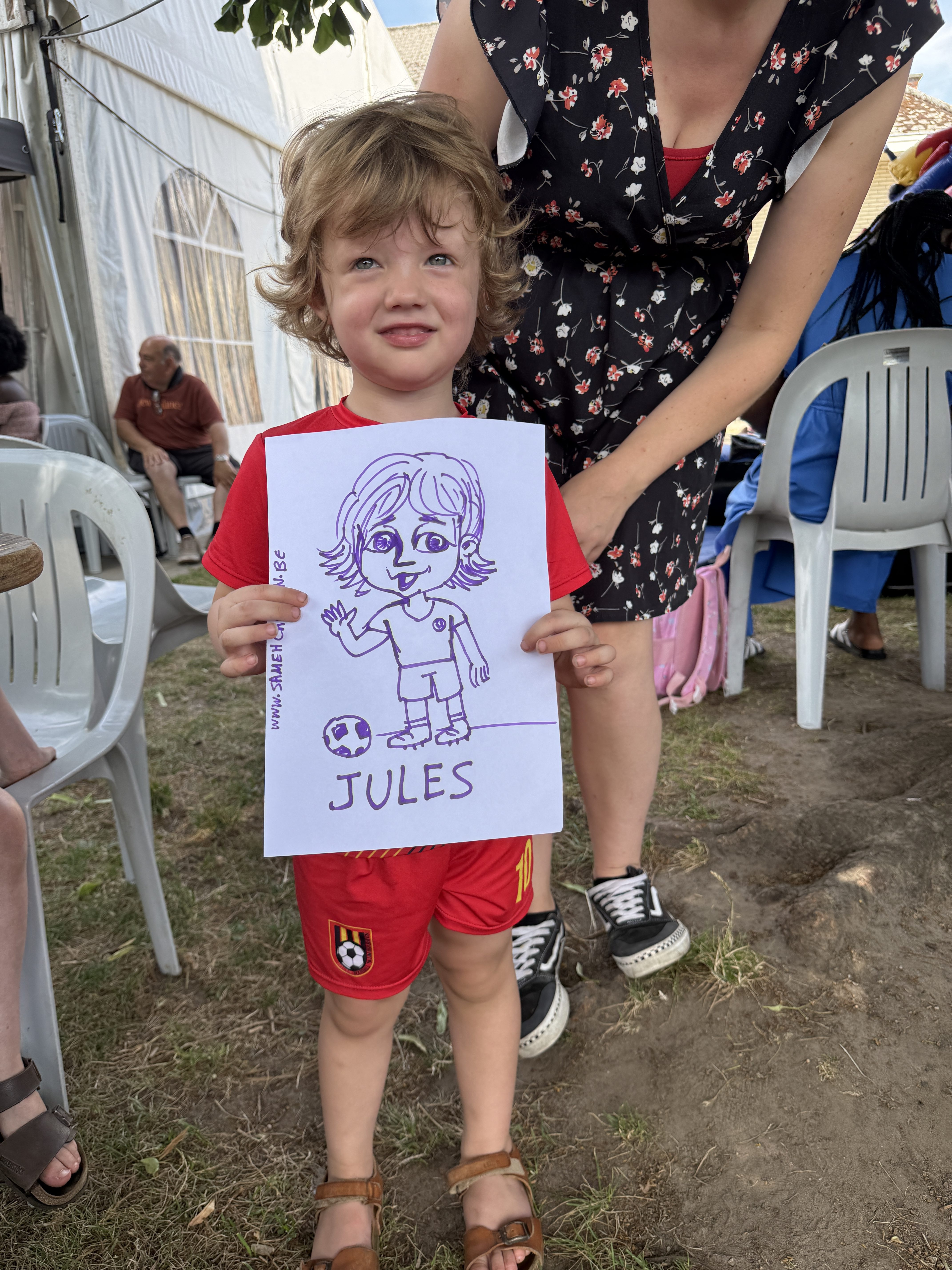 Young child holding a finished live caricature drawing at an outdoor celebration
