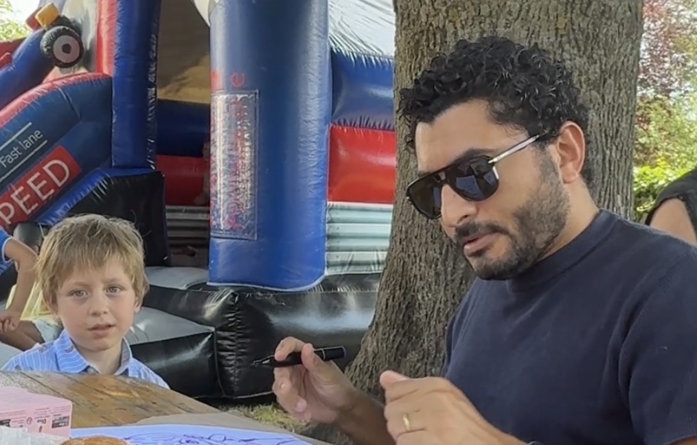 Sameh Samir drawing a live caricature for a child at an outdoor event in Buggenhout