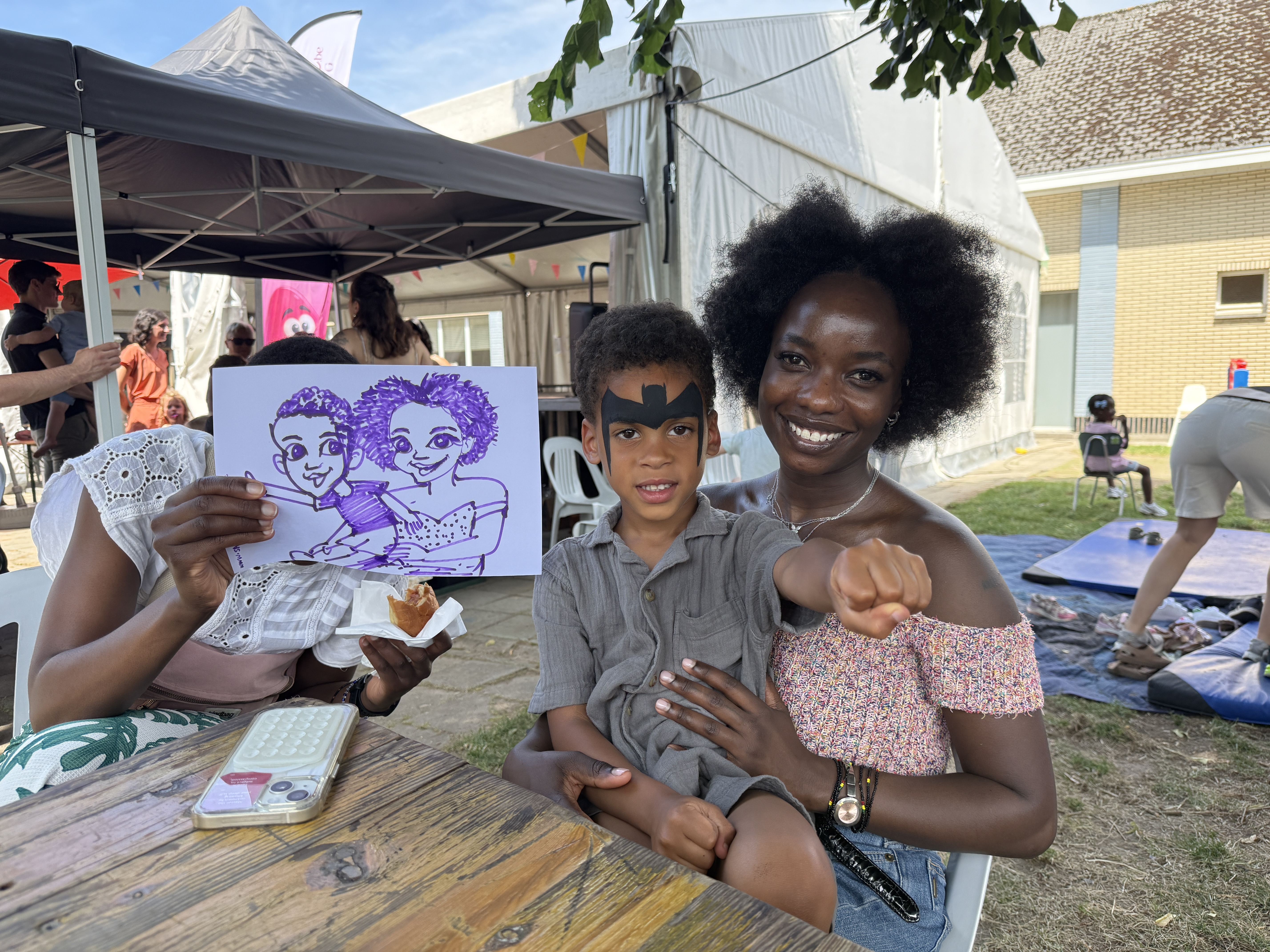 Woman proudly holding a caricature with children at an outdoor family event